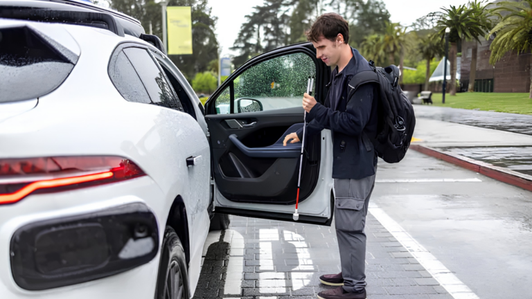 A young man in a dark jacket opens the passenger-side door of a white car in an outdoor parking area, looking down at the door as he opens it. The setting appears to be a paved lot or driveway with green trees or hedges blurred in the background.